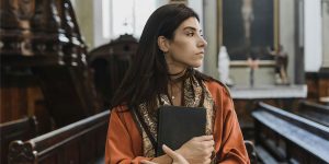 Woman clutching Bible looking pensive in a church.