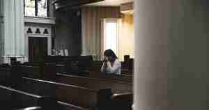 A woman preys in a church pew.