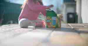 A little girl plays on the floor with a box of chalk.